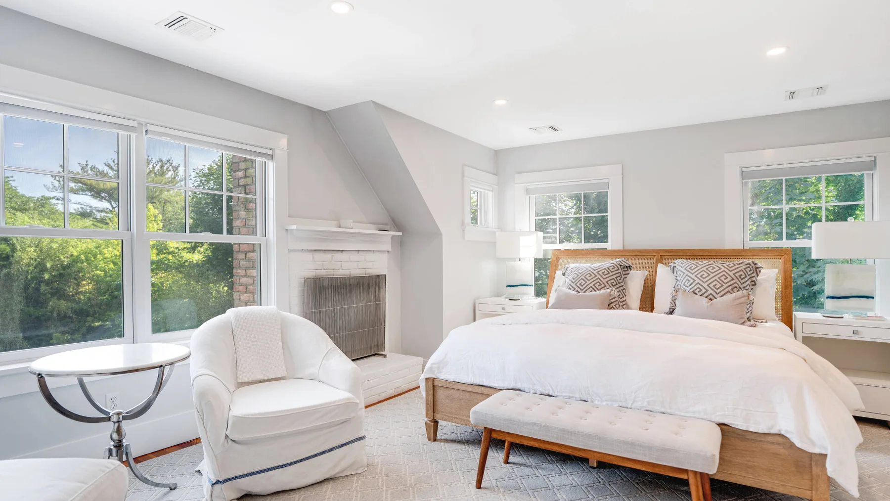 A bright bedroom with a bed, an armchair, and a fireplace.