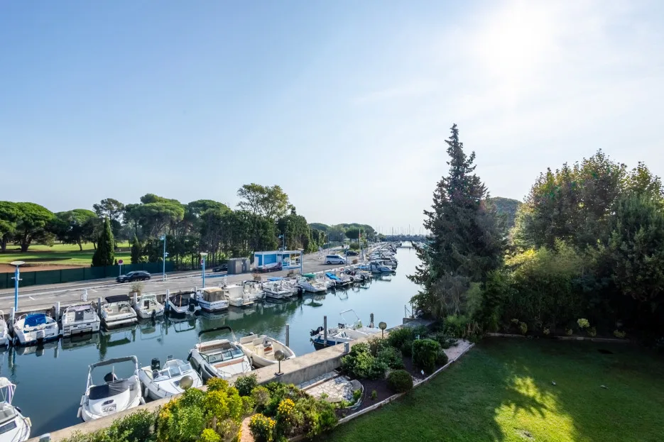 A marina with boats moored along a calm waterway beside a green lawn.