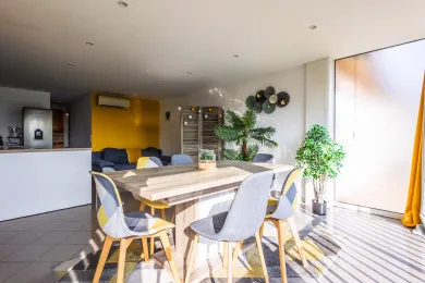 A bright dining area with a wooden table, colorful seating, and large windows.