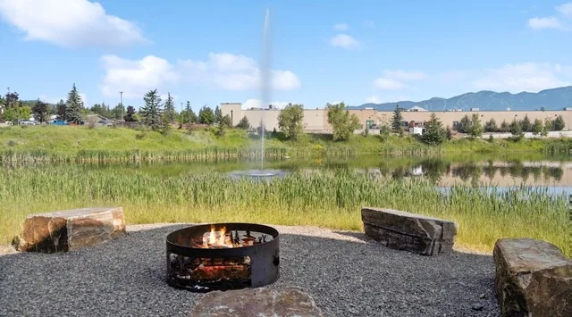 A gravel seating area with a fire pit overlooks a reed-lined pond.