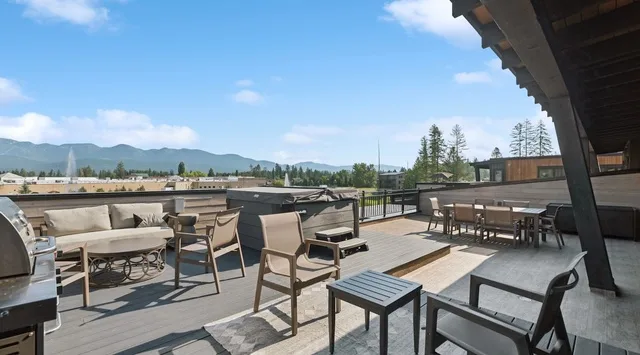 An outdoor deck with seating and dining tables overlooks a mountain landscape.