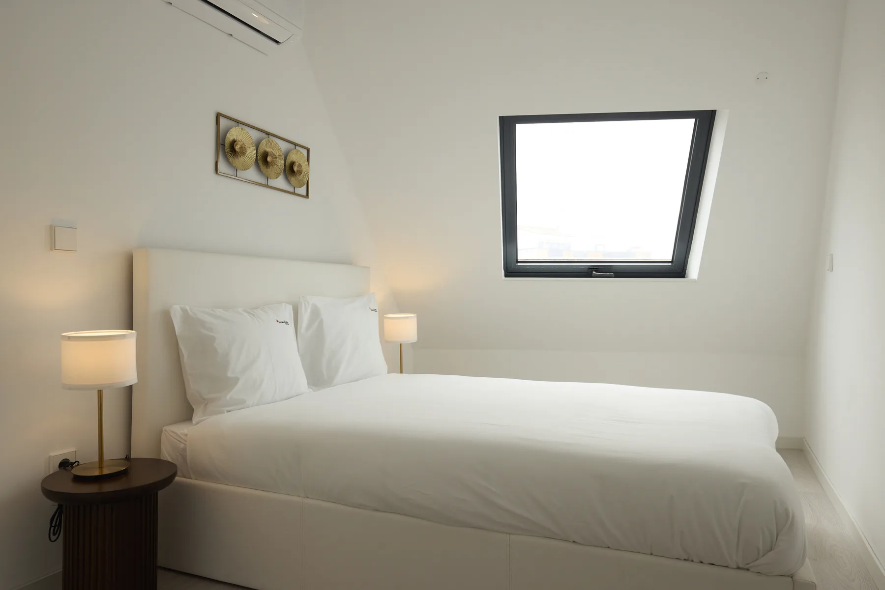 A bedroom with a neatly made bed and a slanted skylight.