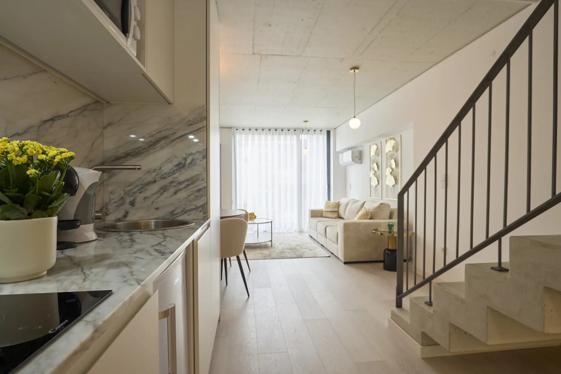 A bright living room with a sofa, dining table, and staircase.