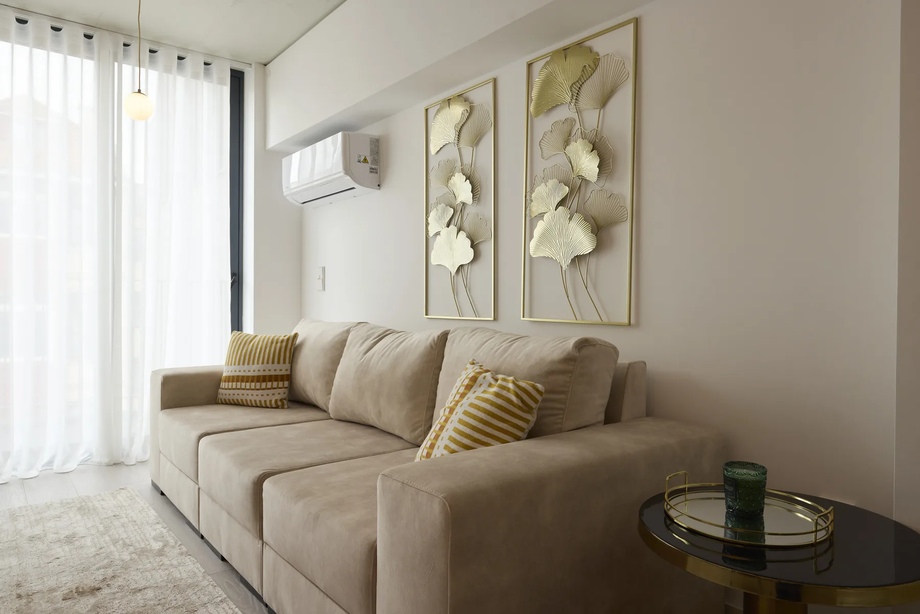 A bright living room with beige seating, sheer curtains, and floral wall art.