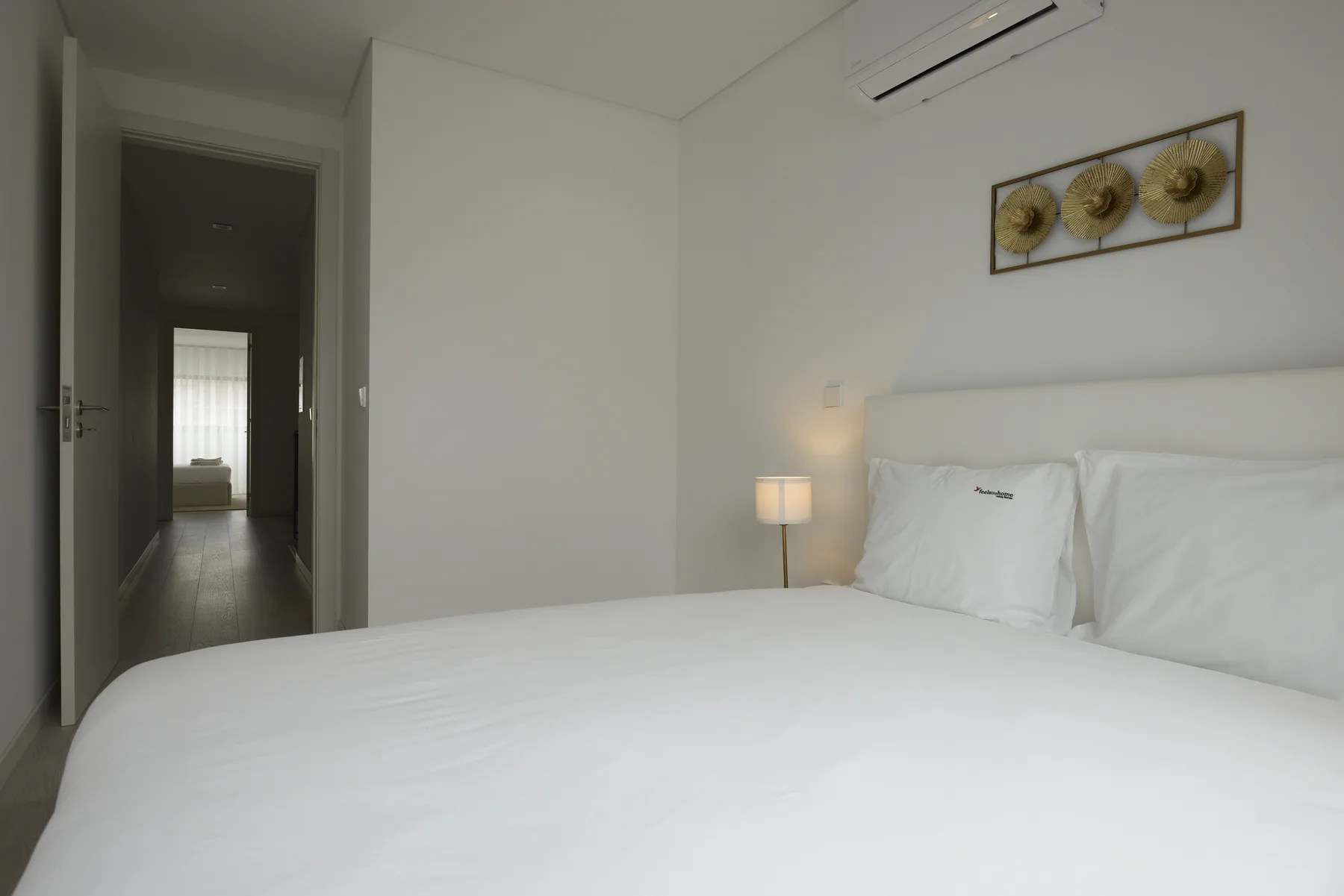 A bedroom with a white bed, bedside lamp, and framed wall art.