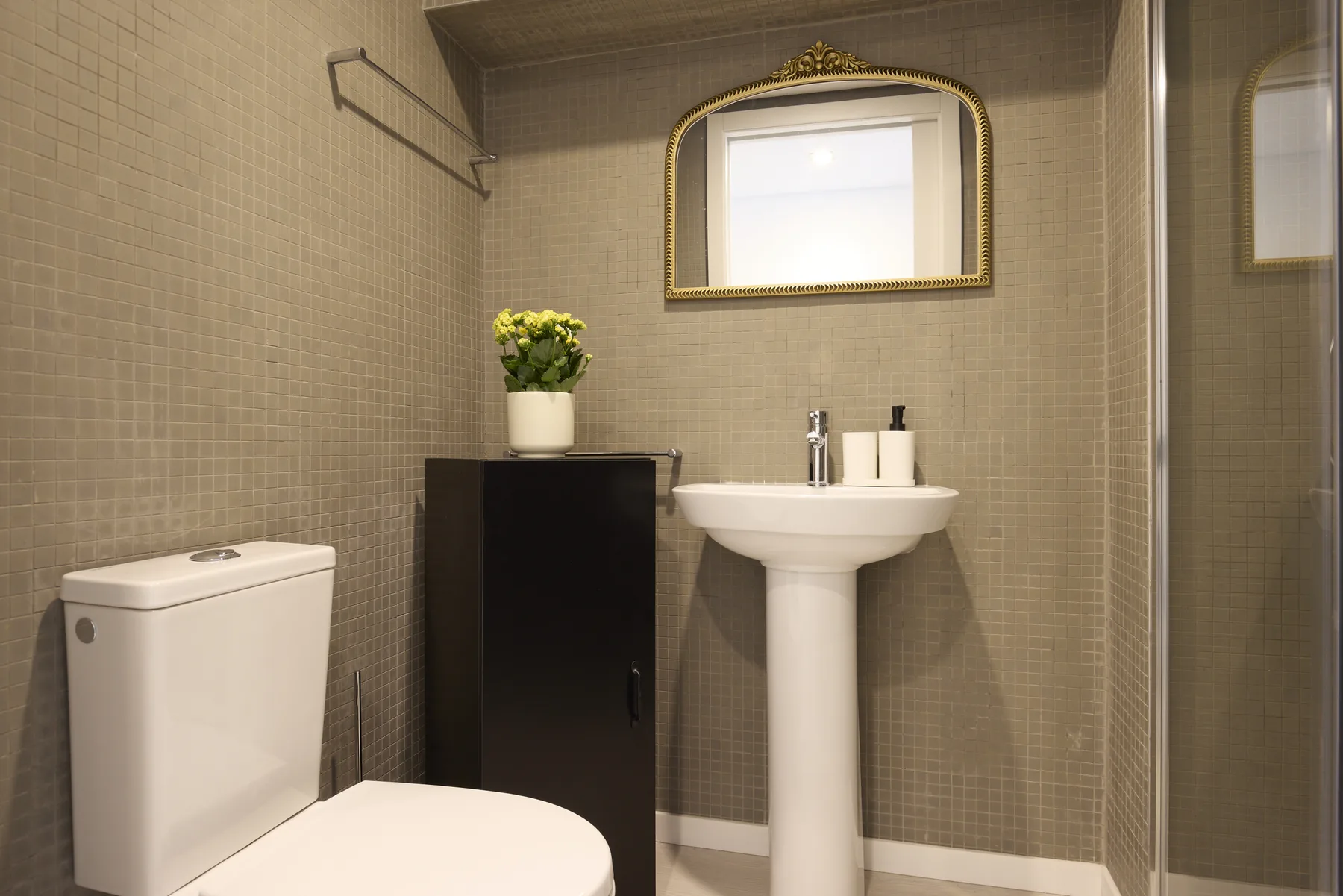 A tiled bathroom with a pedestal sink and a gold-framed mirror.