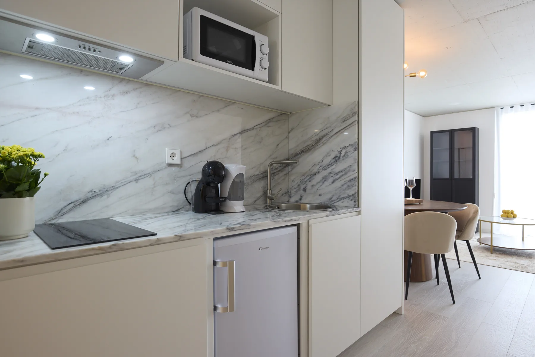 A modern kitchen with a countertop, microwave, and coffee maker opens onto a dining area.
