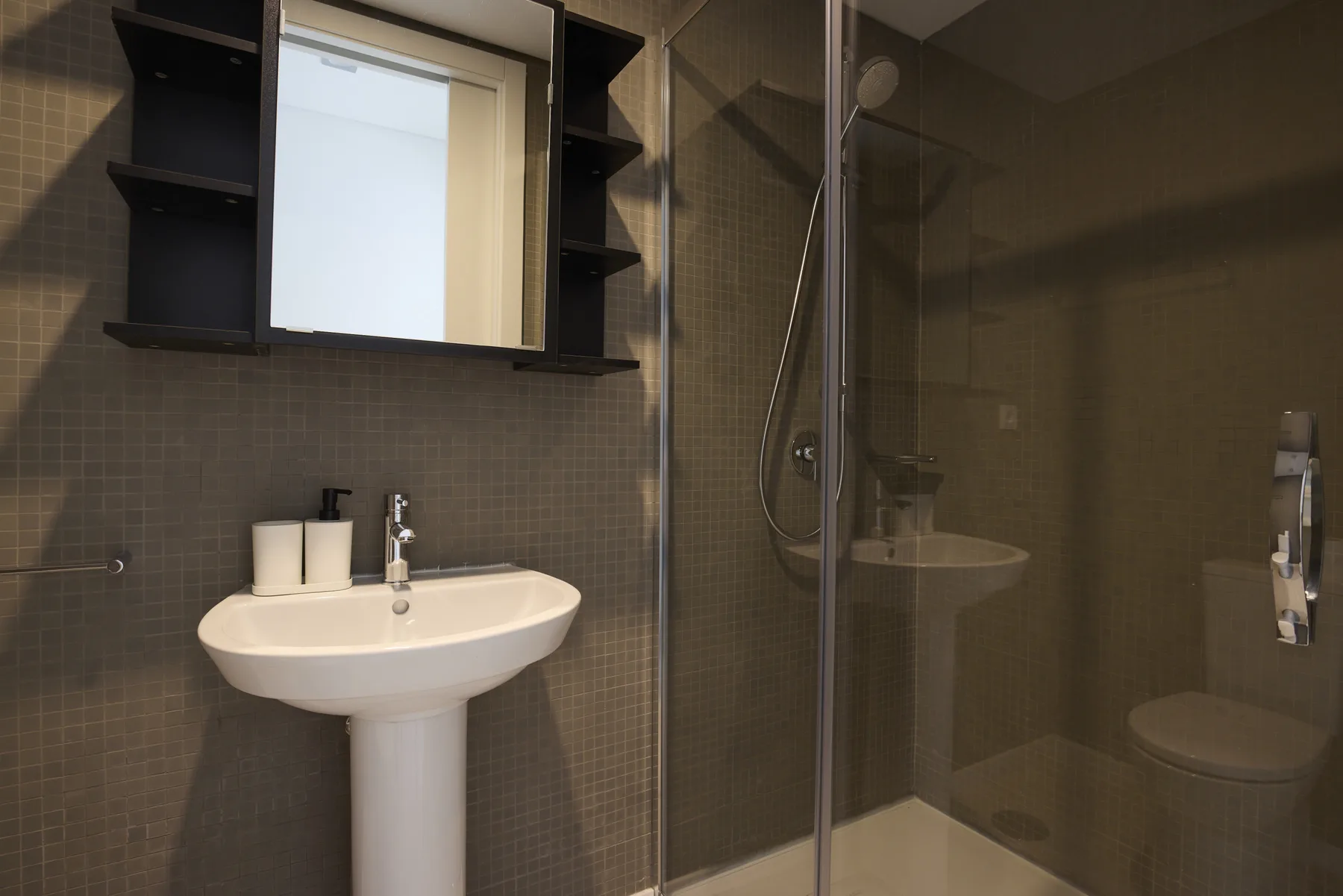 A tiled bathroom with a pedestal sink, mirror, and shower.