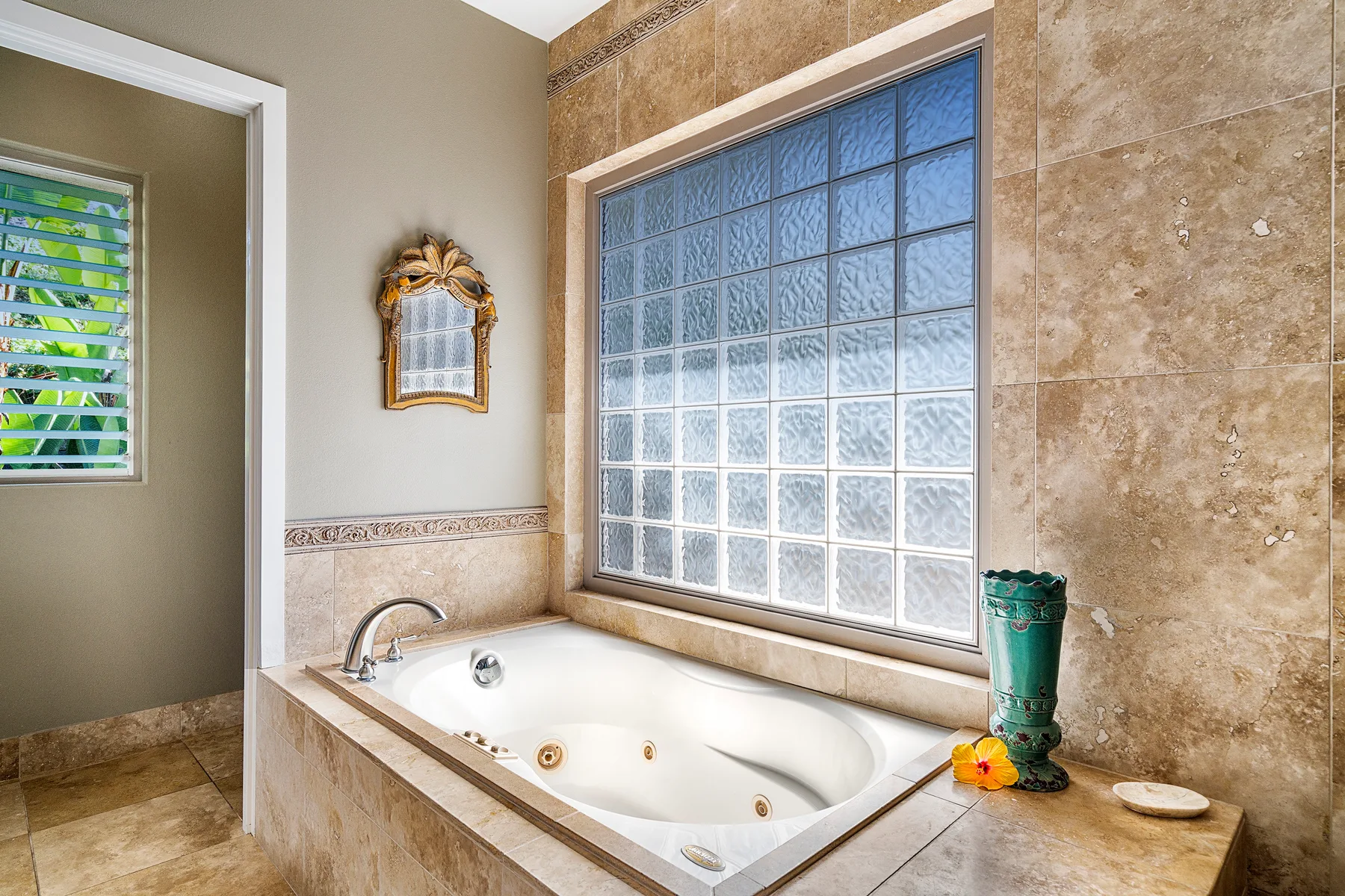 A tiled bathroom features a corner bathtub beside a glass-block window.