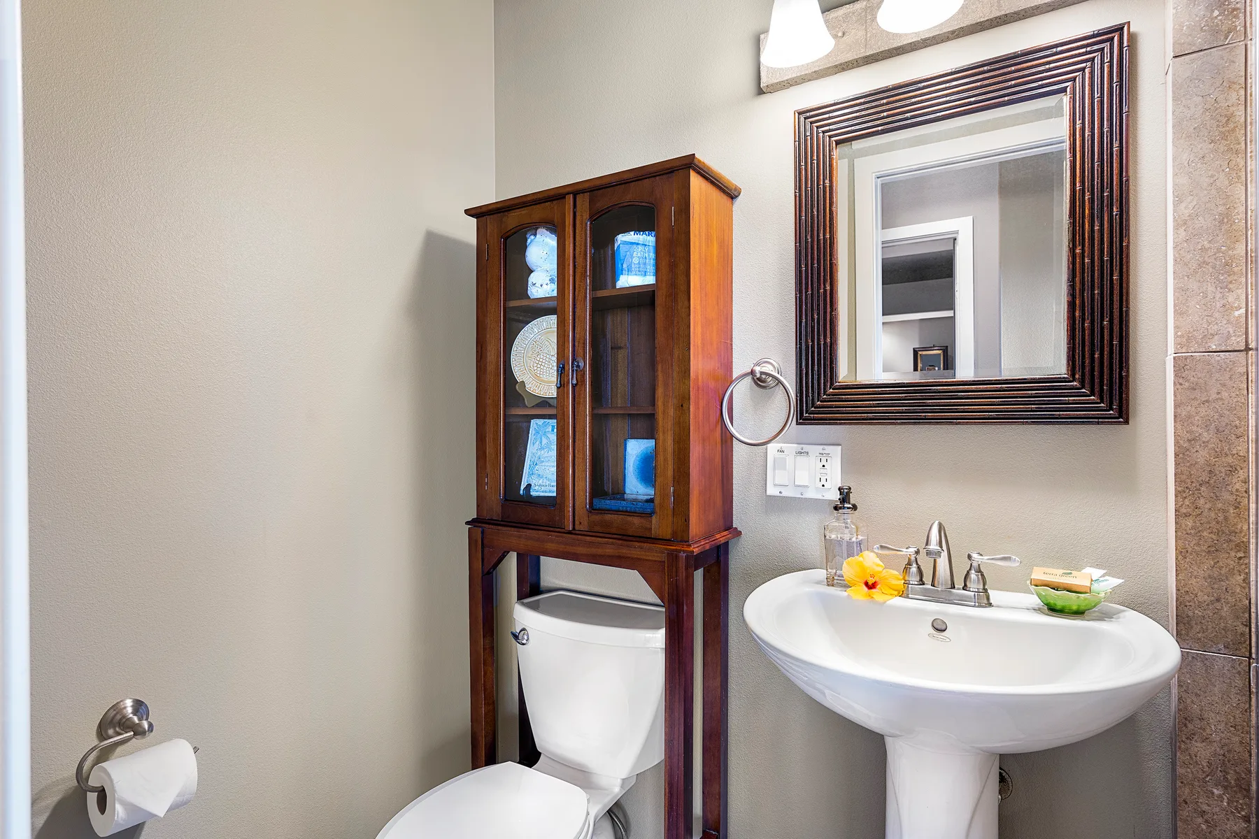 A bathroom with a sink, mirror, and wooden cabinet beside the toilet.