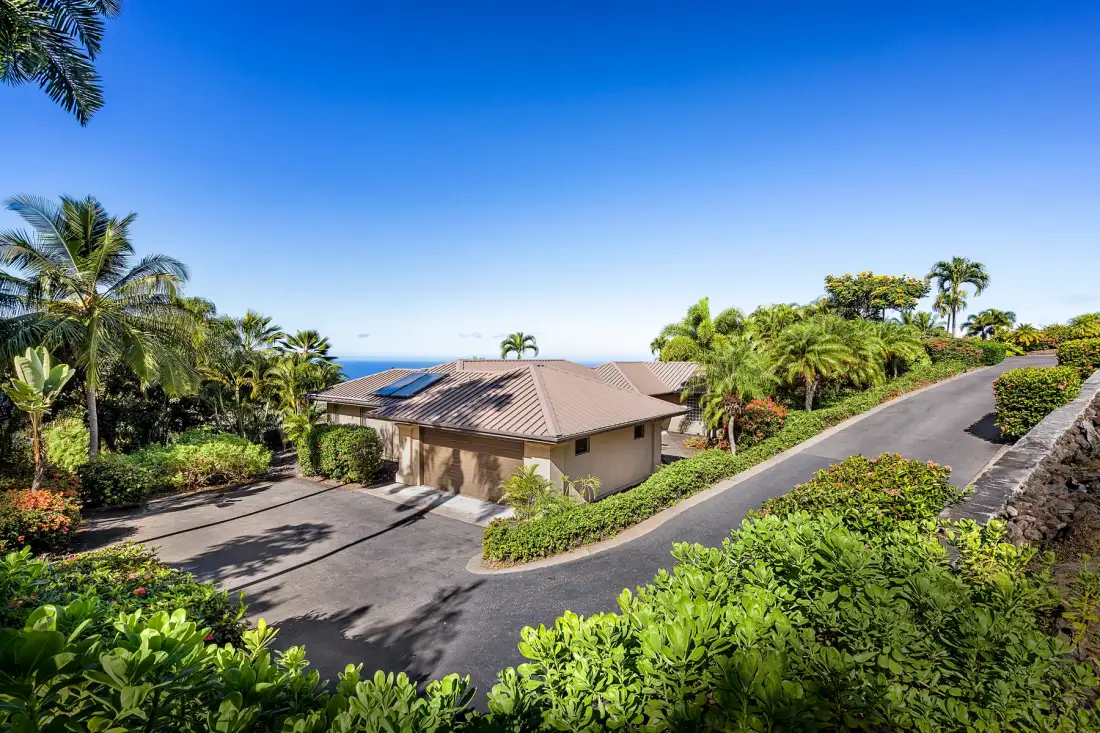 A tropical property entrance with a paved driveway winding past a low building.