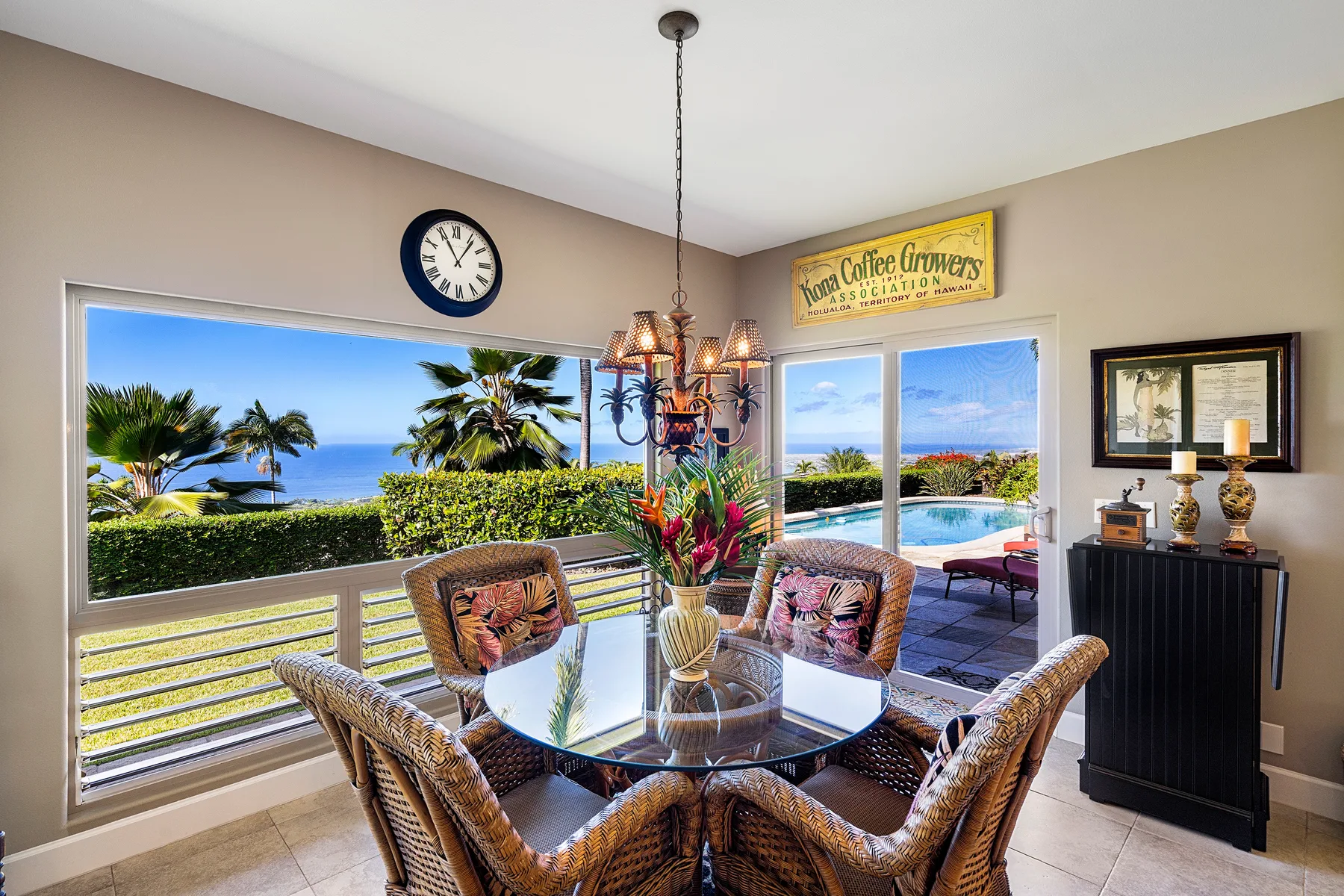 A dining area with woven seating and a glass table overlooks a patio and ocean.