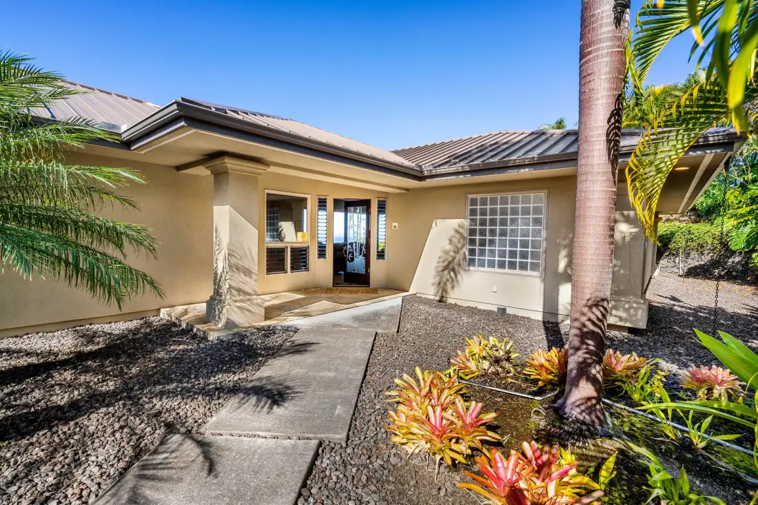 A single-story house with a paved walkway and tropical landscaping.