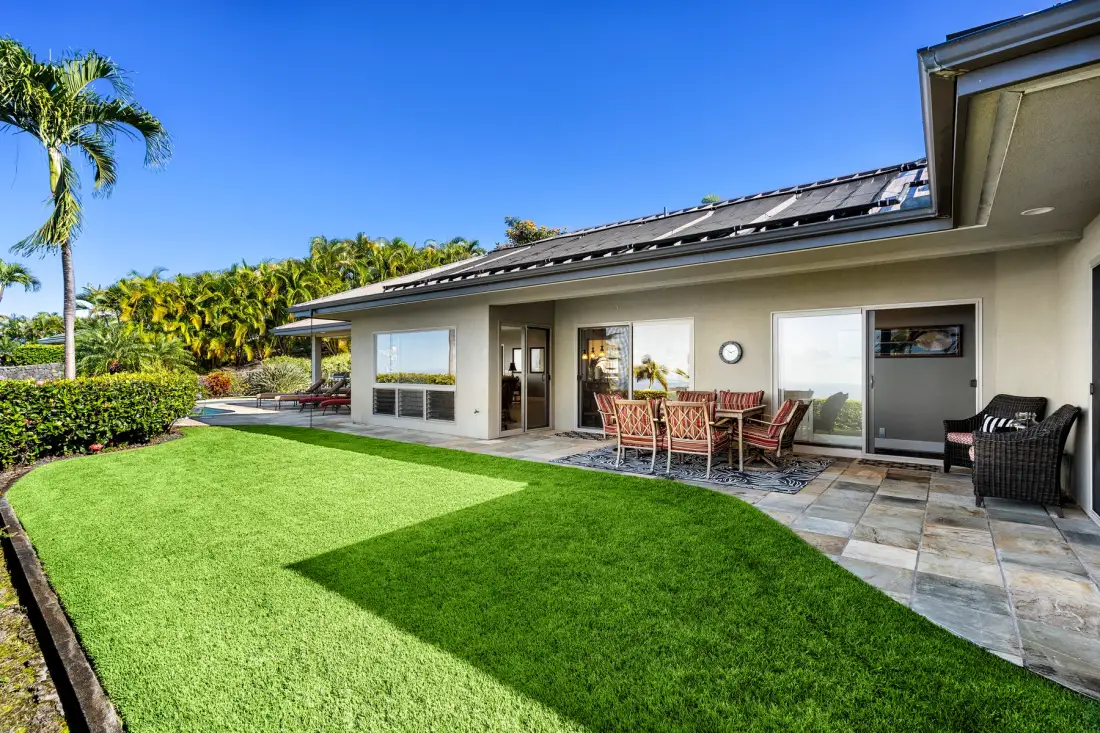 A single-story house opens onto a green lawn and a tiled patio with outdoor seating.