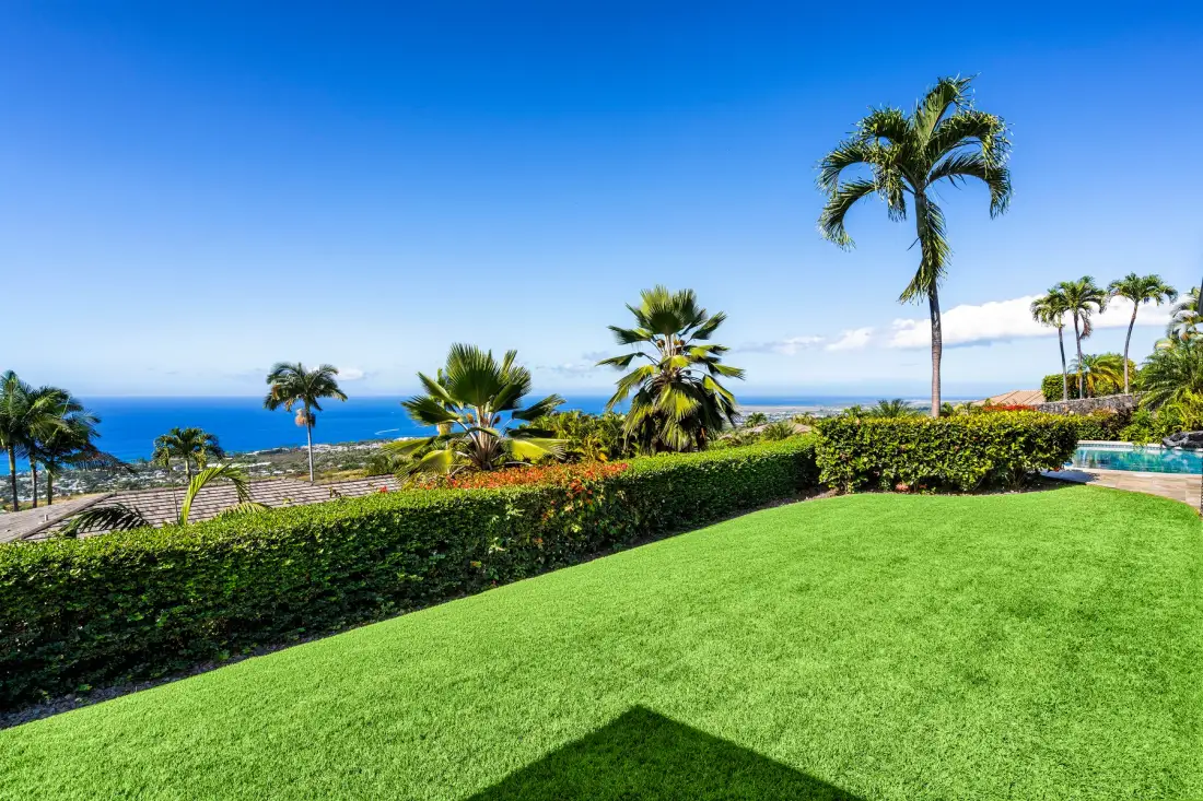 A landscaped lawn and palm trees overlook the ocean under a clear blue sky.