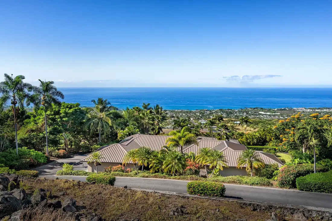 A low-rise building sits among tropical greenery overlooking the ocean.