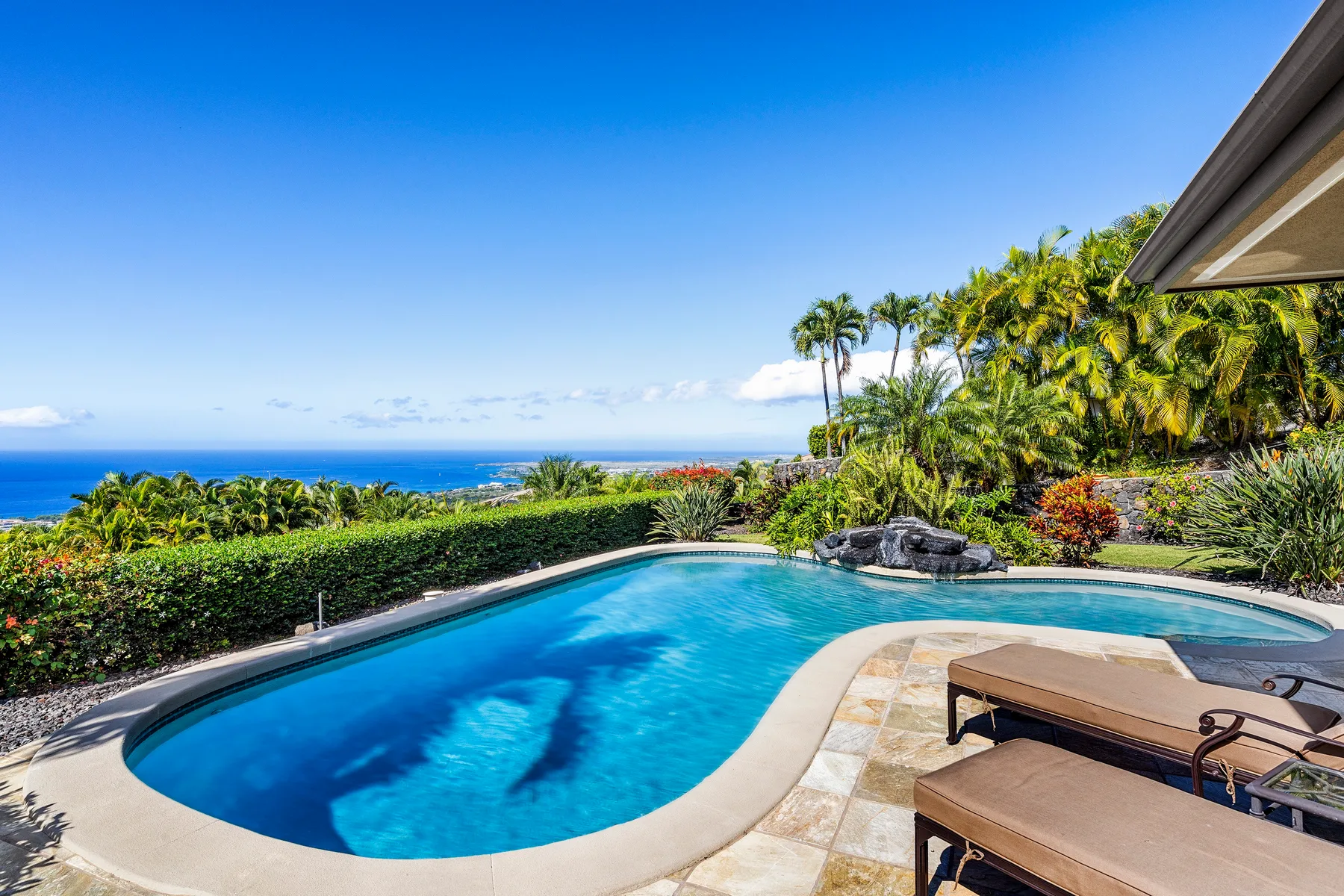A curved swimming pool overlooks the ocean, with lounge seating beside it.