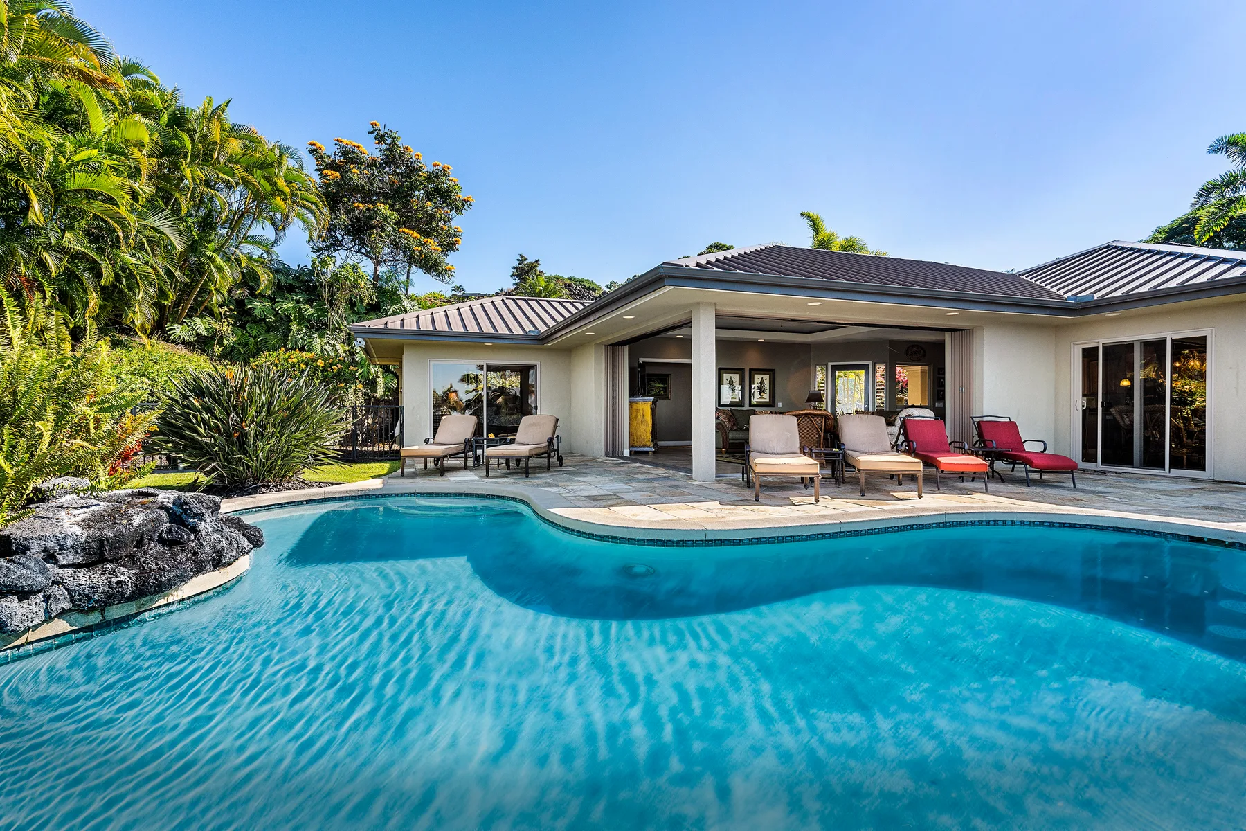 A swimming pool curves around the patio of a single-story house.