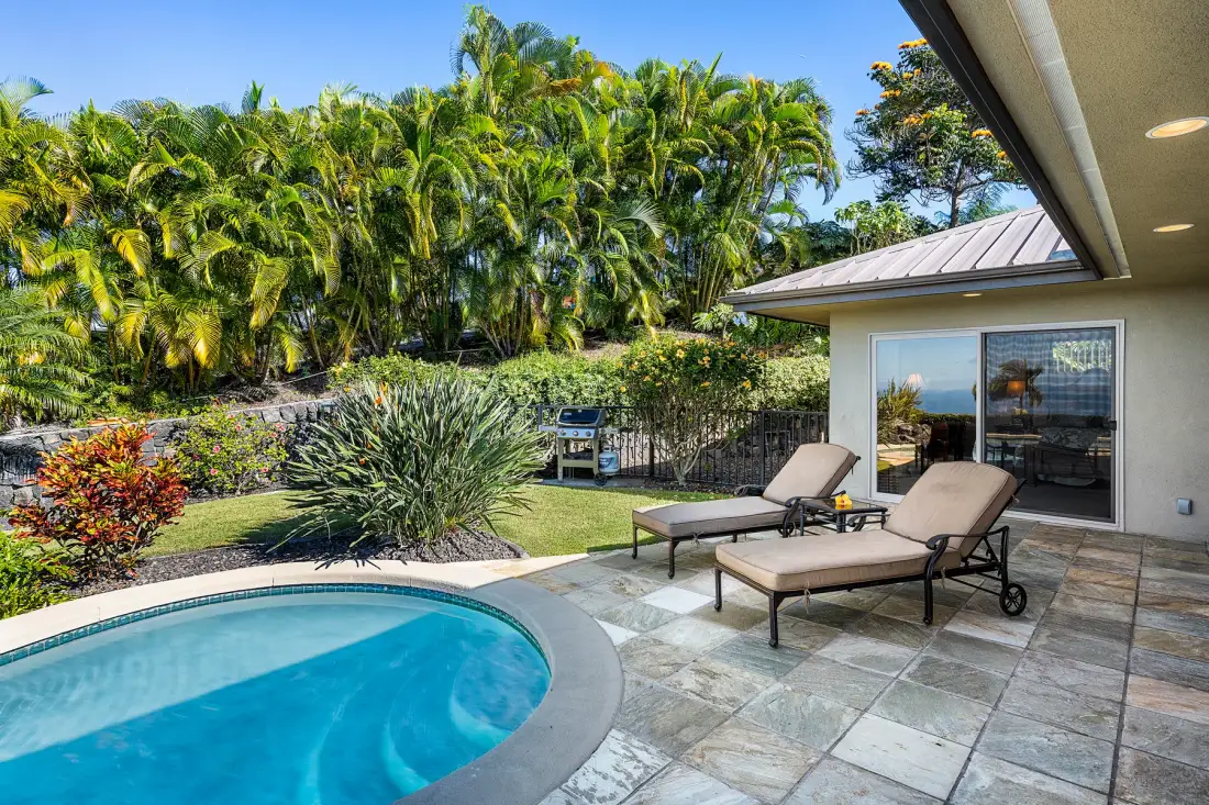 A pool patio with reclining loungers beside a landscaped garden.