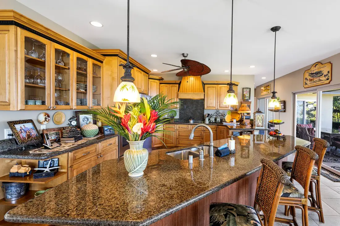 A spacious kitchen with wooden cabinetry, stone counters, and a flower arrangement.