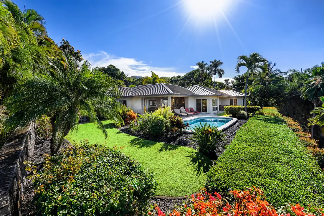 A sunlit garden surrounds a house and outdoor swimming pool.