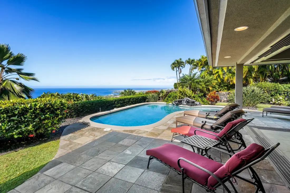 A patio with a swimming pool and lounge seating overlooks the ocean.