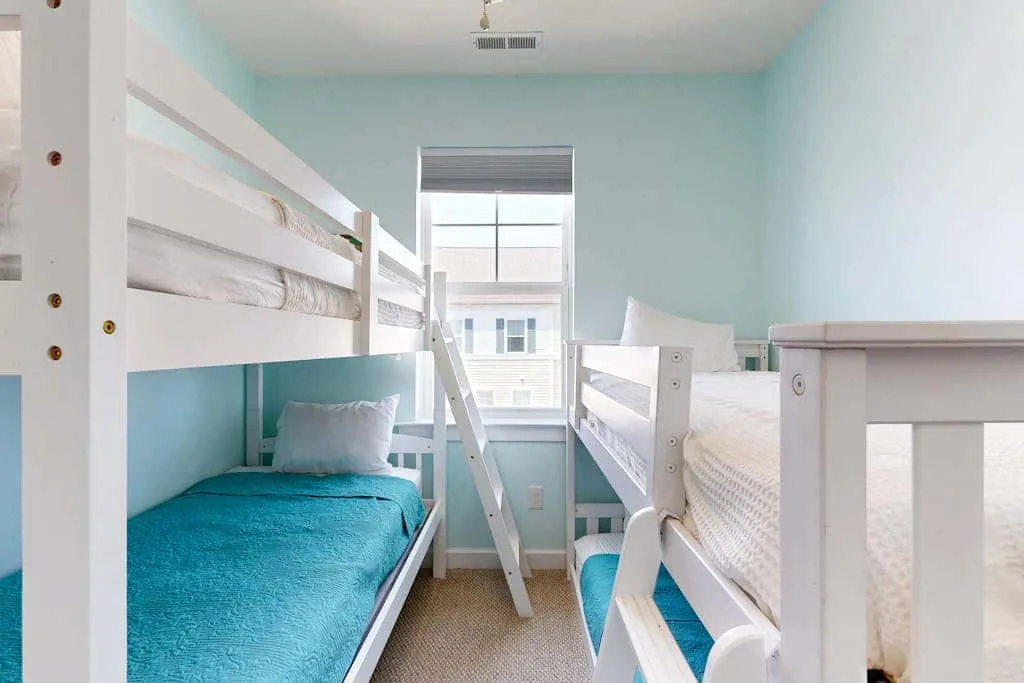 A bright bedroom with two white bunk beds and turquoise bedding.