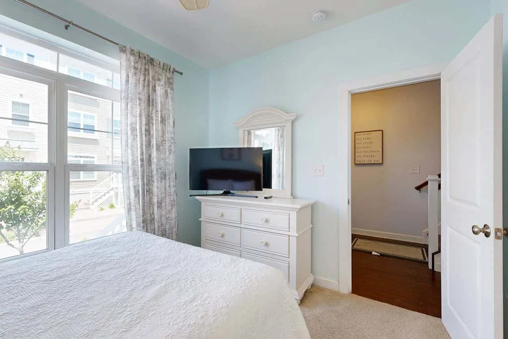 A bedroom with a television on a dresser beside a large window.