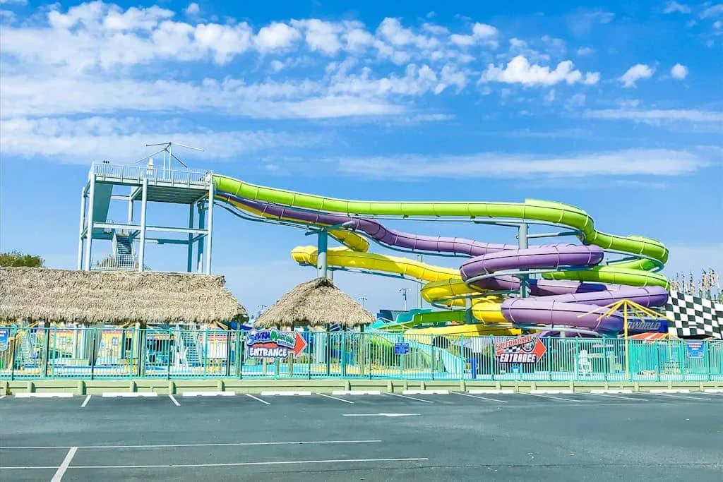 A colorful water slide complex rises behind a fenced outdoor pool area.