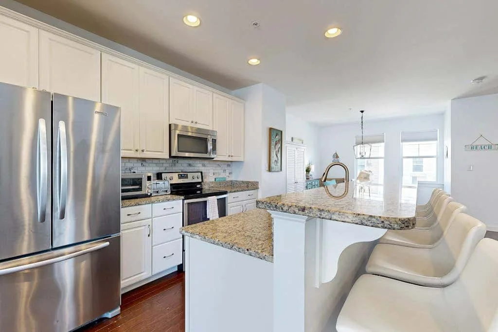 A bright kitchen with stainless steel appliances and a central island with seating.