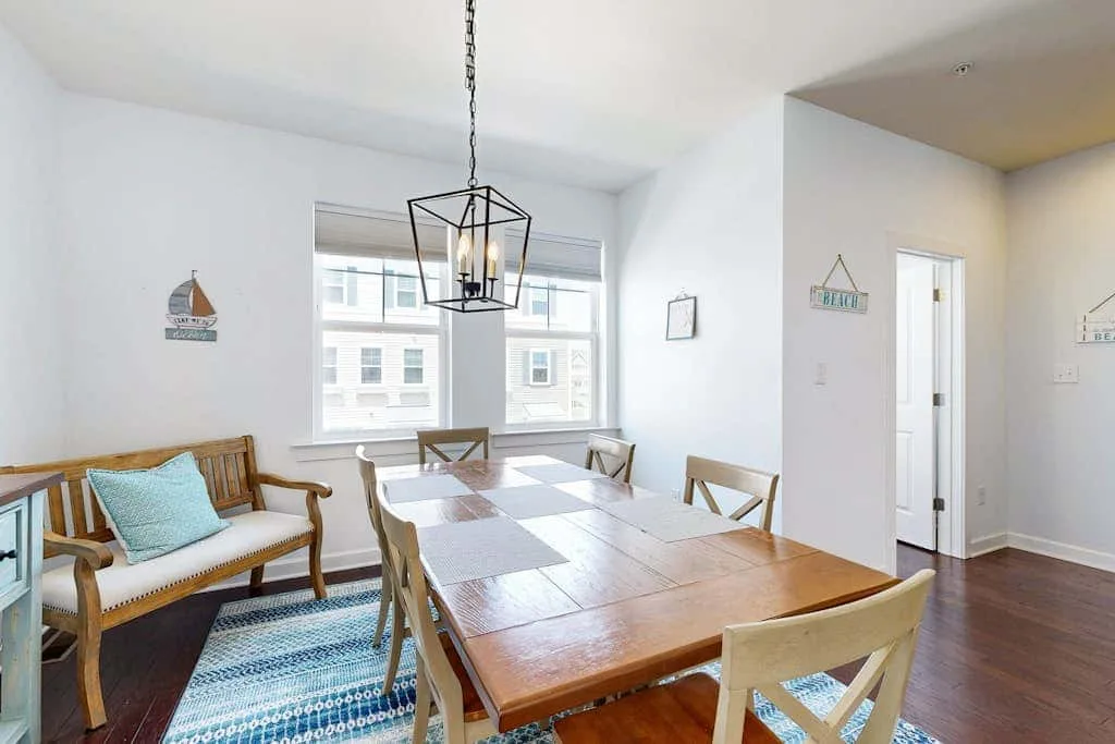 A bright dining area with a wooden table, seating, and large windows.