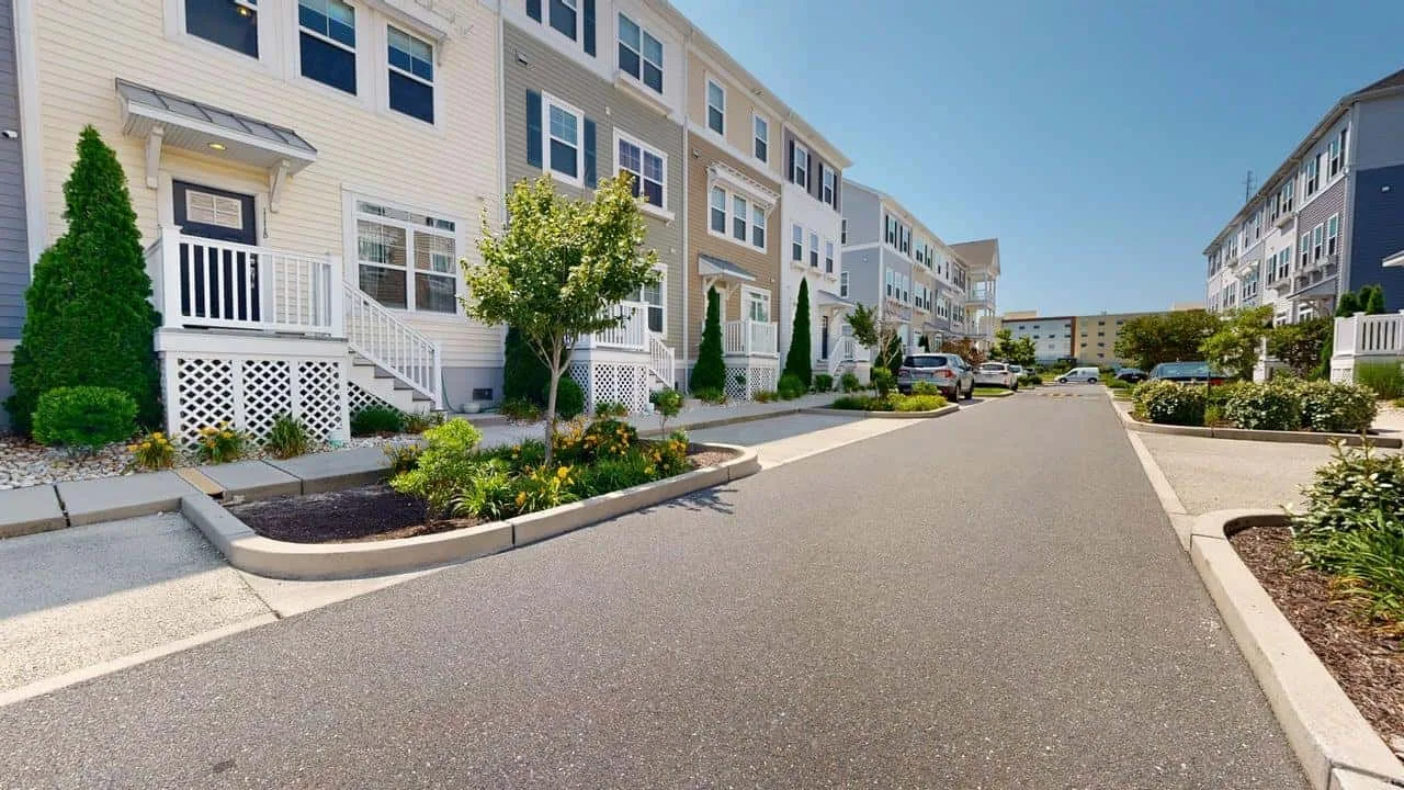 A paved street runs between rows of multi-story residential buildings and landscaped planting beds.