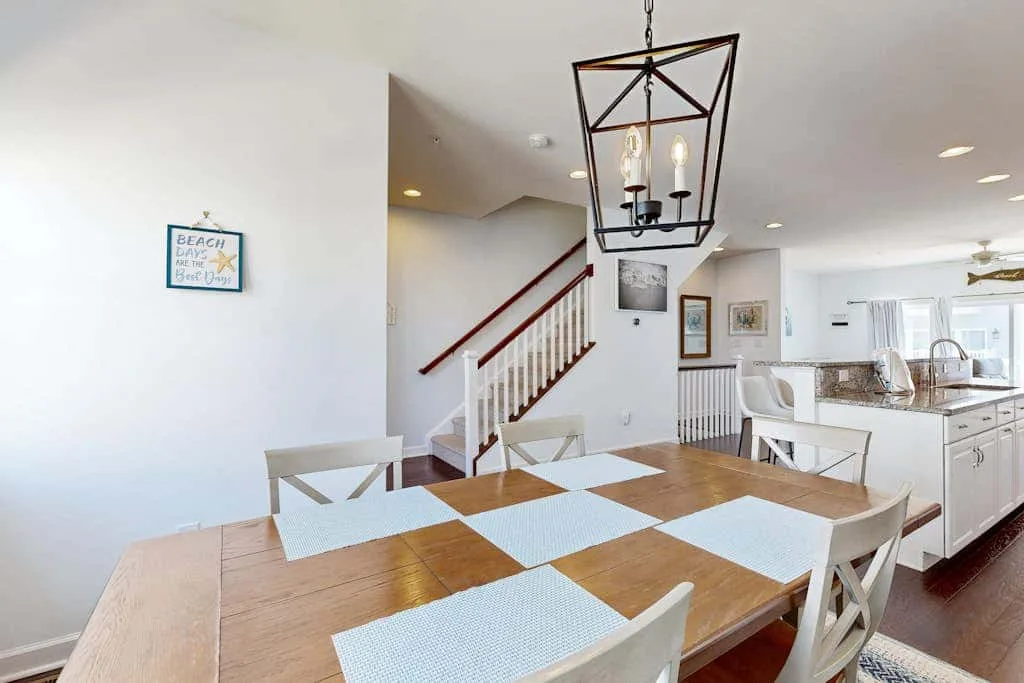A dining area with a wooden table and an open kitchen beyond.