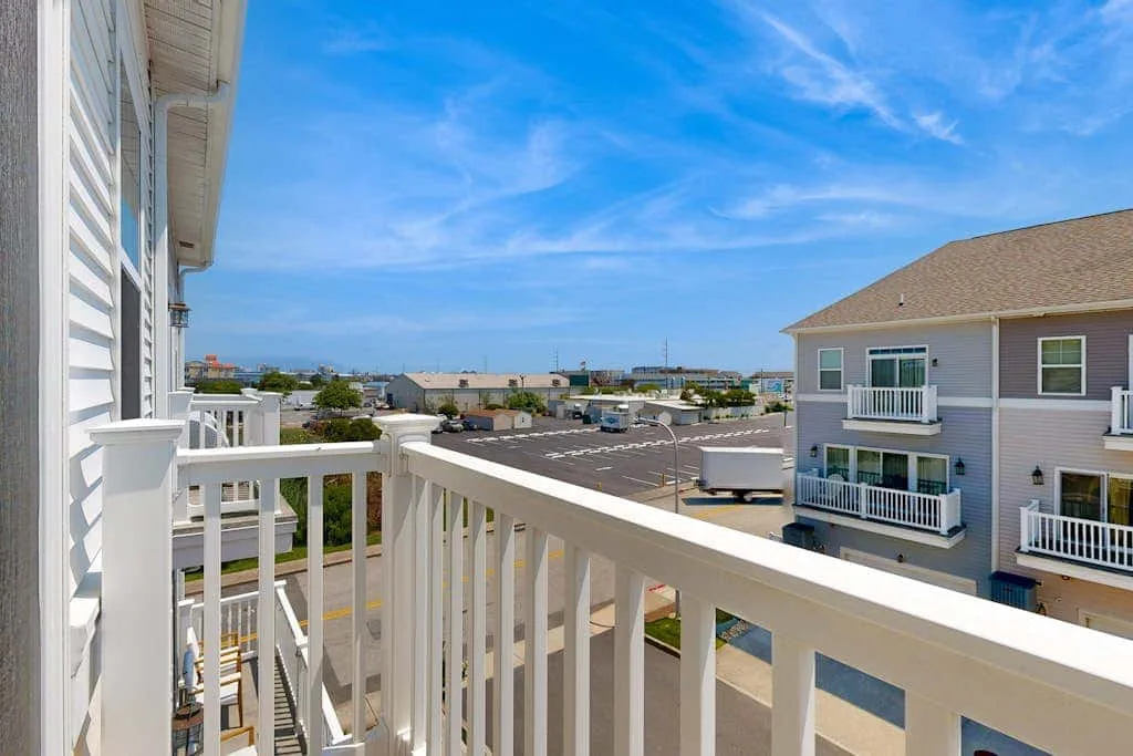 Balcony overlooking neighboring buildings and a parking area beneath a blue sky.