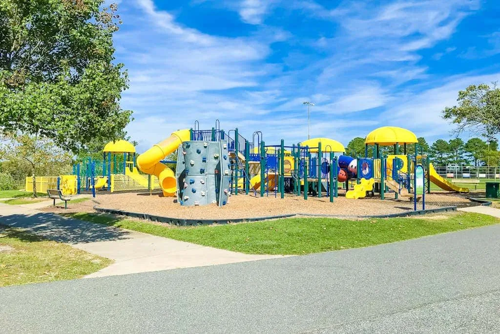 A colorful outdoor playground with slides and climbing equipment sits beside a paved path.
