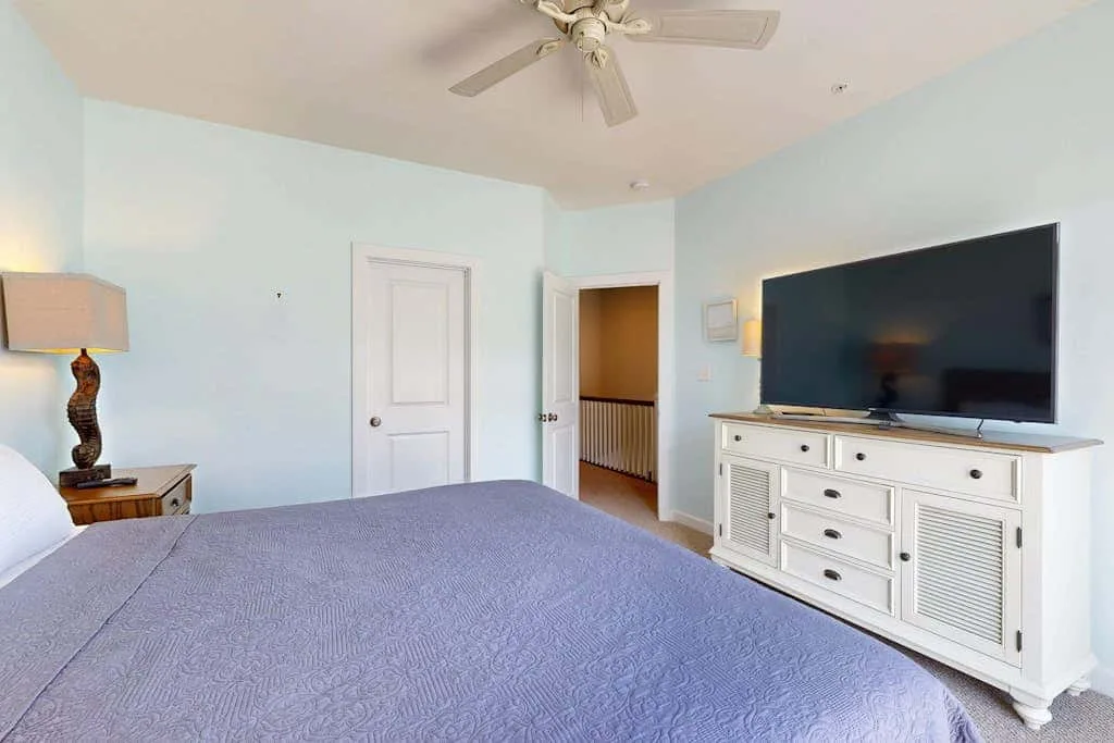 A bedroom with a bed, ceiling fan, and television on a white dresser.