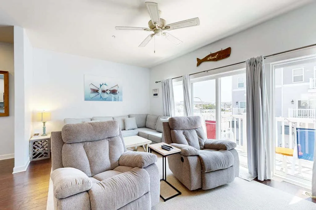 A bright living room with reclining seating beside large windows and glass doors.