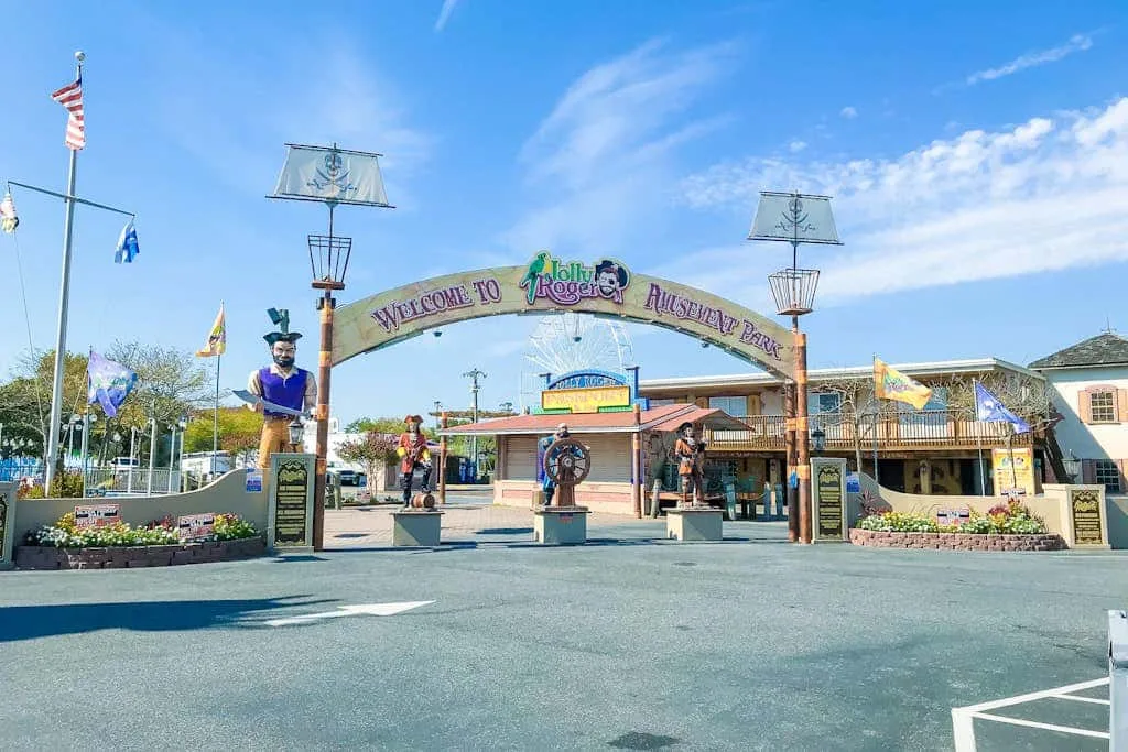 An amusement park entrance with a welcome arch and colorful storefronts.