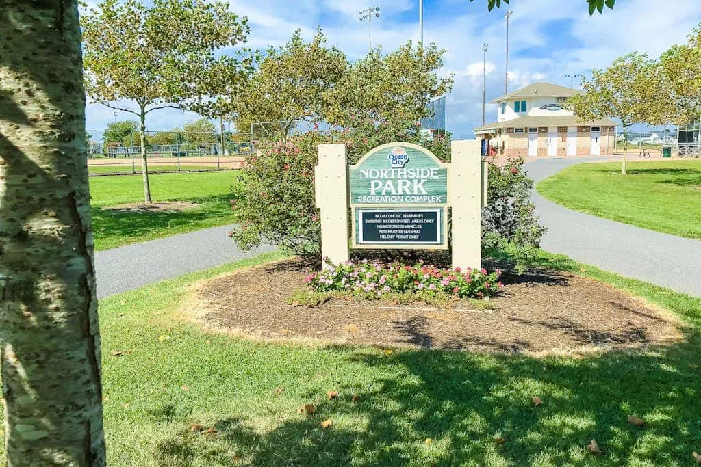 A park entrance sign stands beside a landscaped flower bed and walking path.