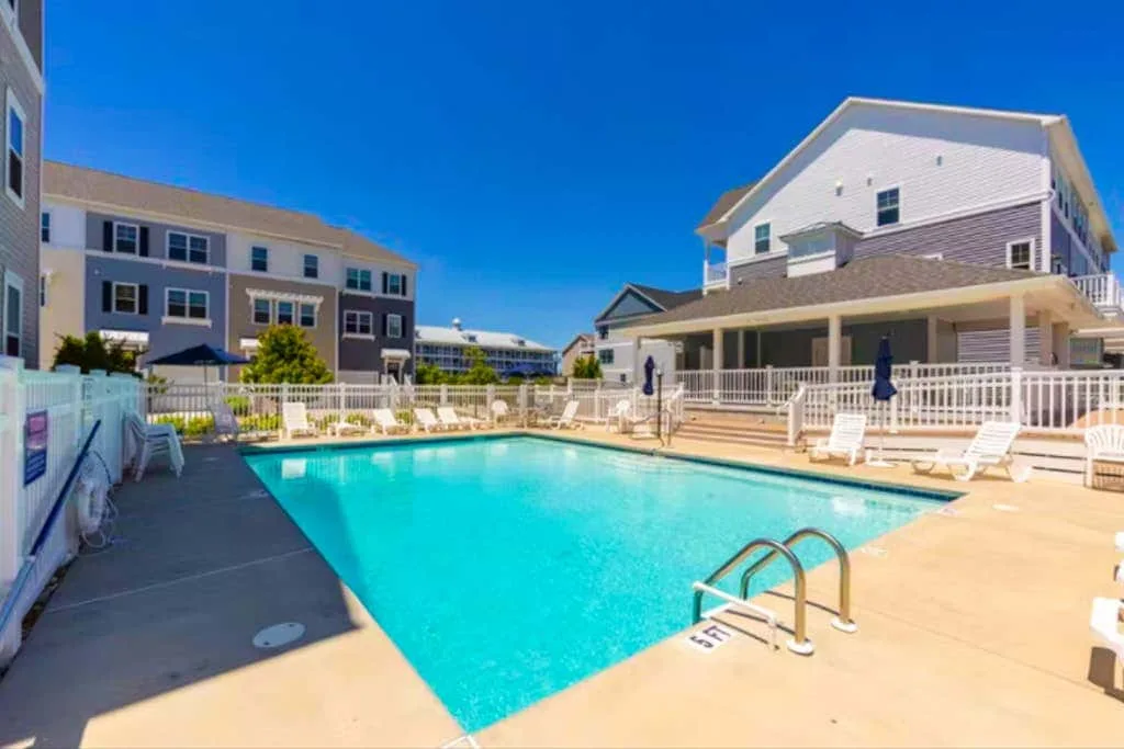 An outdoor swimming pool sits among multi-story buildings under a clear blue sky.