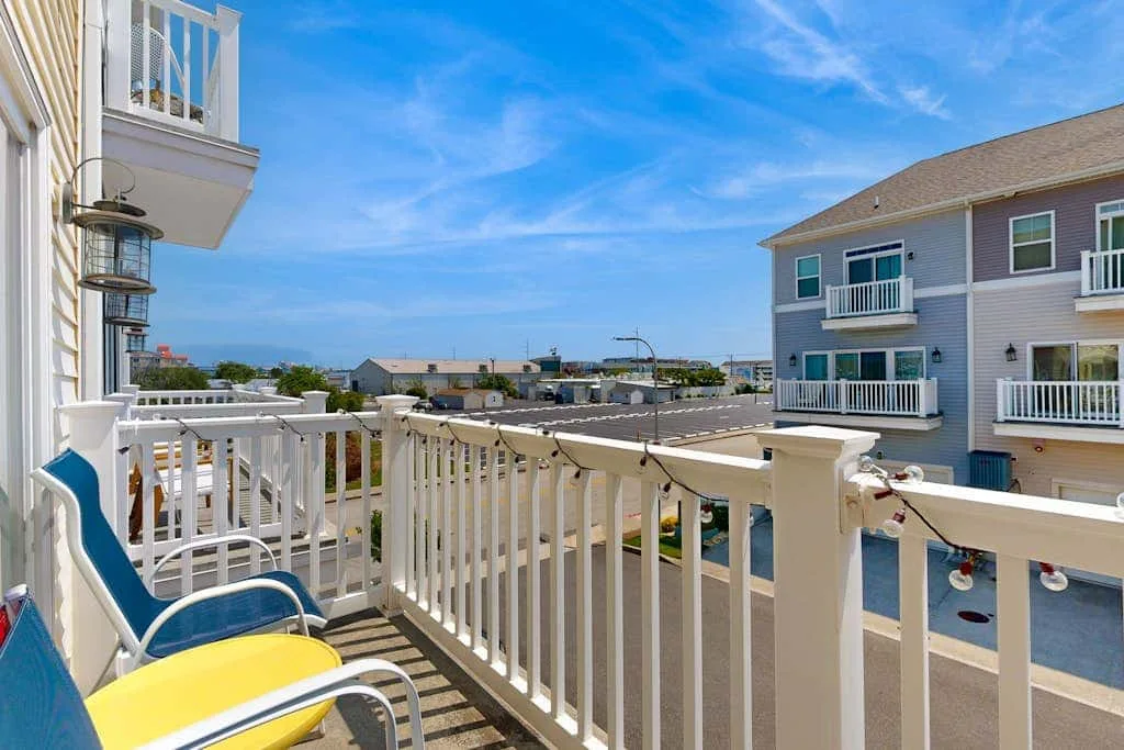 A balcony with white railings overlooks nearby buildings beneath a blue sky.