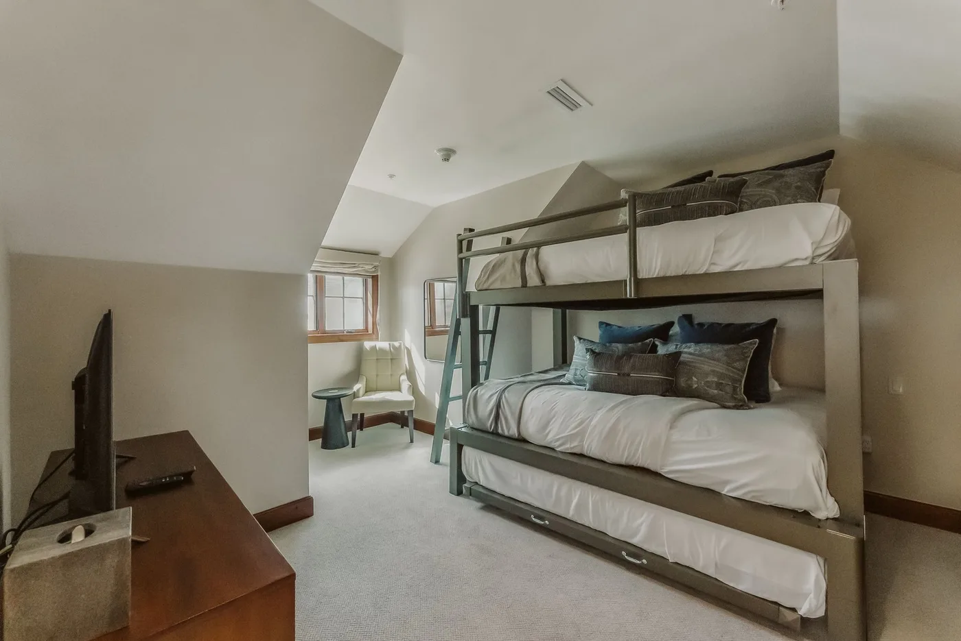 A bedroom with bunk beds, white bedding, and a chair near the window.