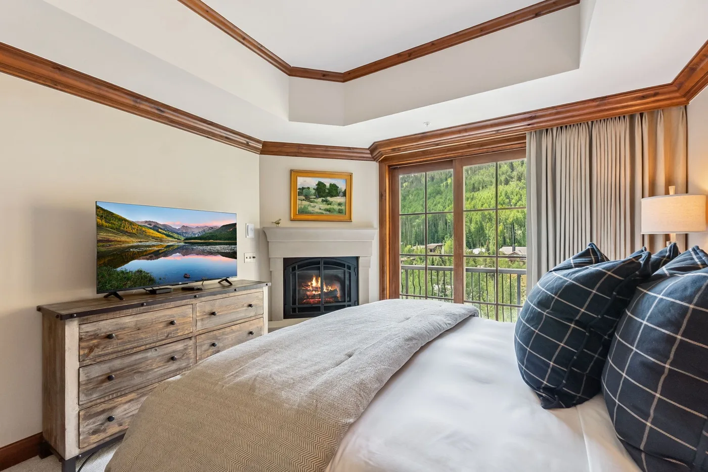 A bedroom with a bed, fireplace, and large windows overlooking greenery.