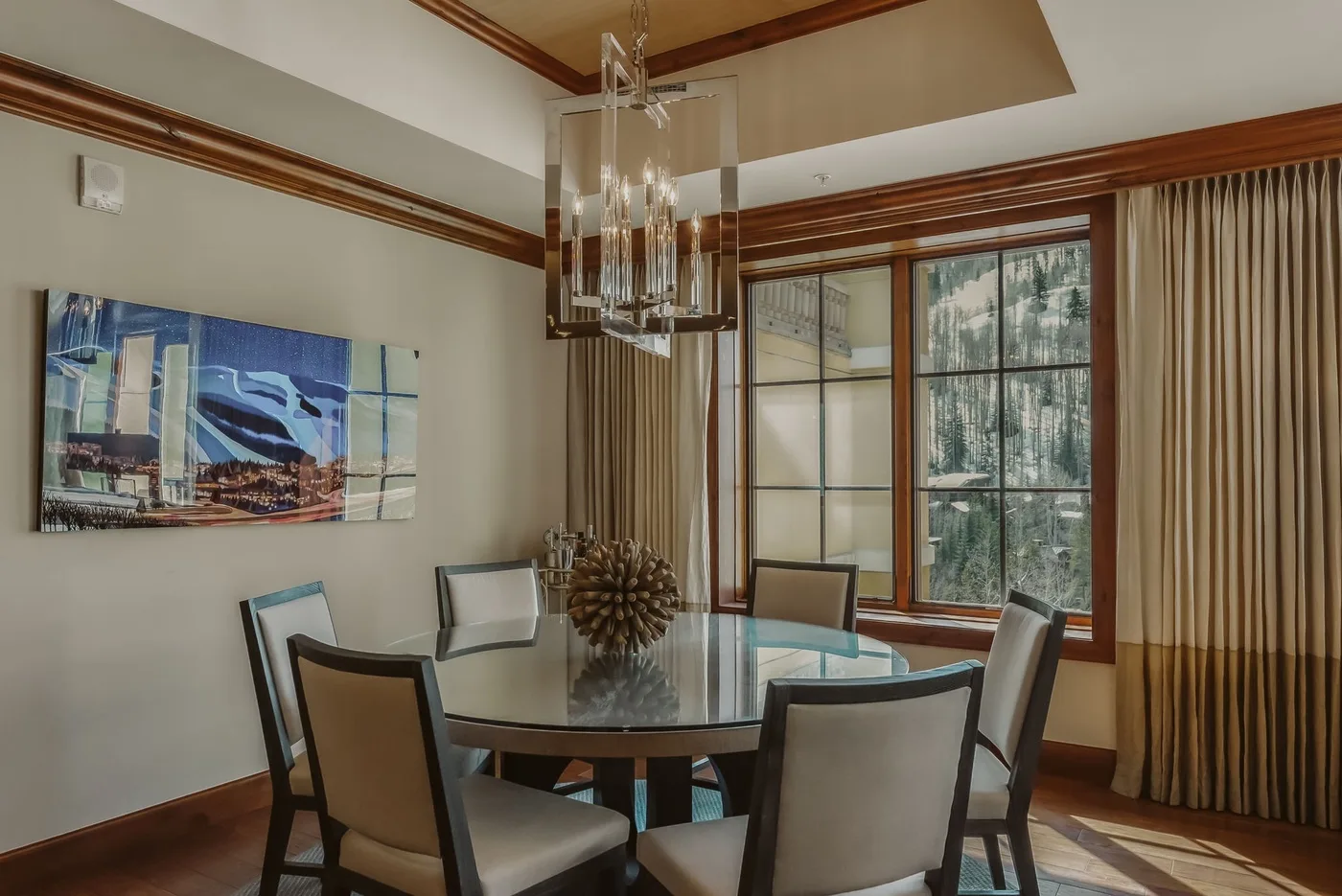 A dining area with a round glass table, upholstered seating, and tall windows.