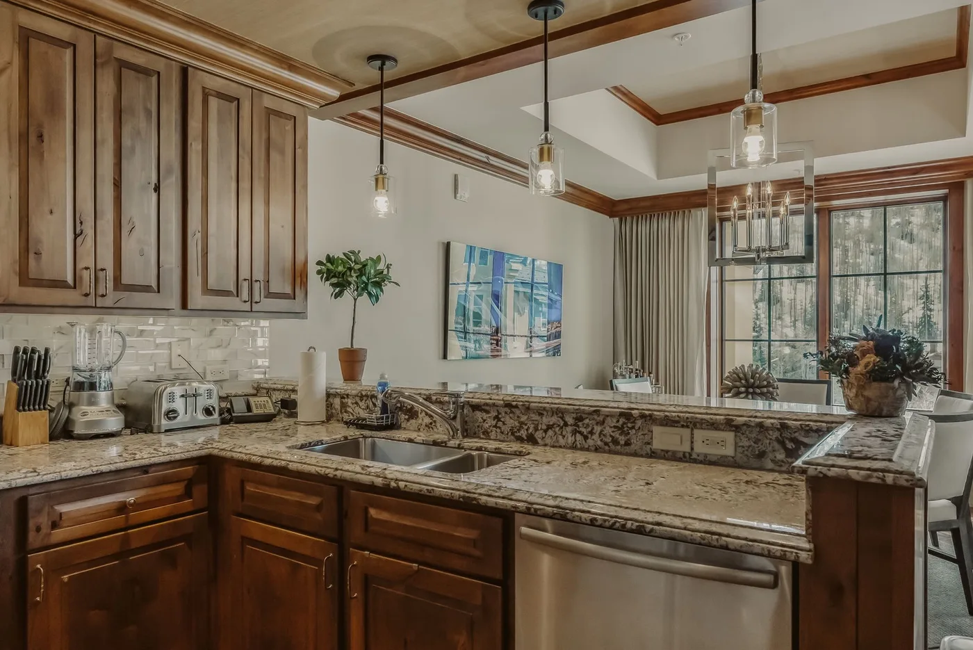 A spacious kitchen with wooden cabinetry, stone countertops, and hanging pendant lights.
