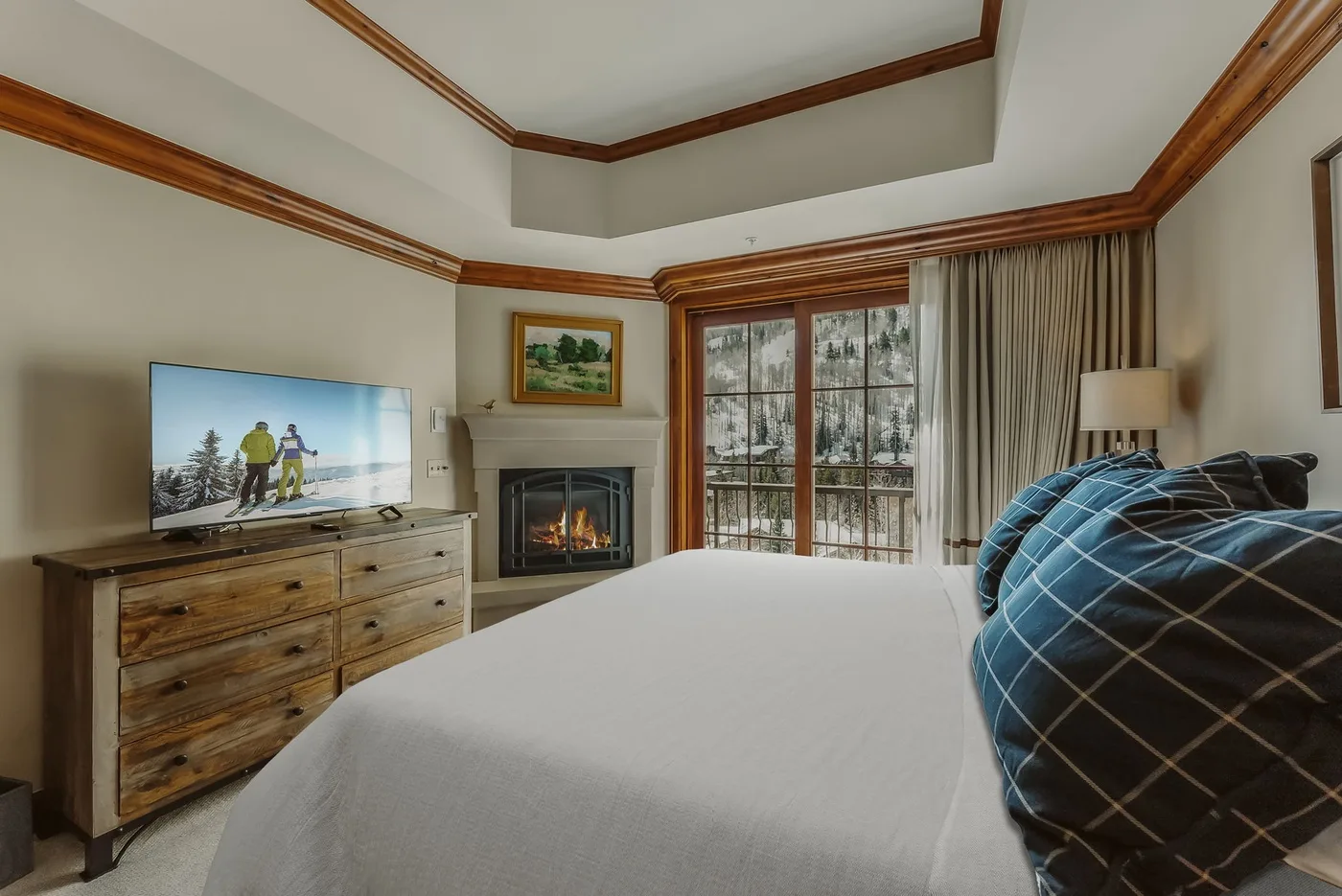 A bedroom with a bed, a television, and a fireplace beside large windows.