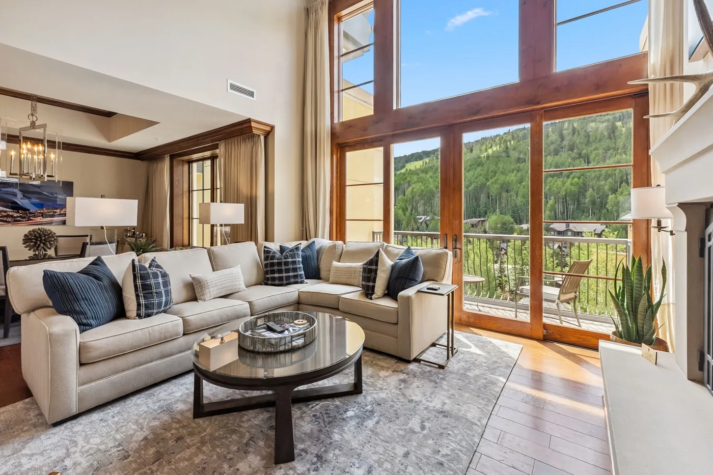 A bright living room with seating beside large windows overlooking a forested hillside.