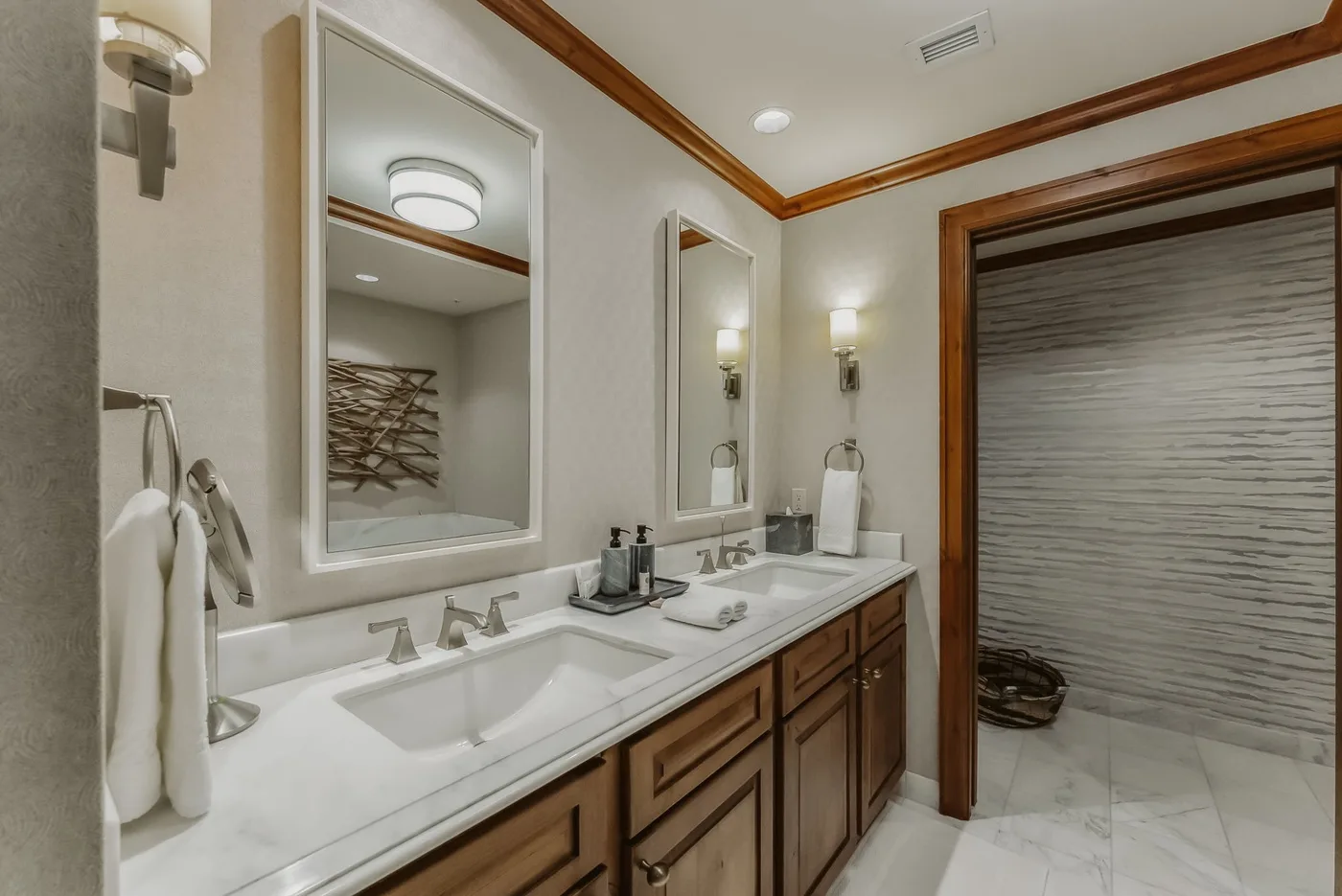 A bathroom vanity with a long counter, sinks, mirrors, and a shower area.