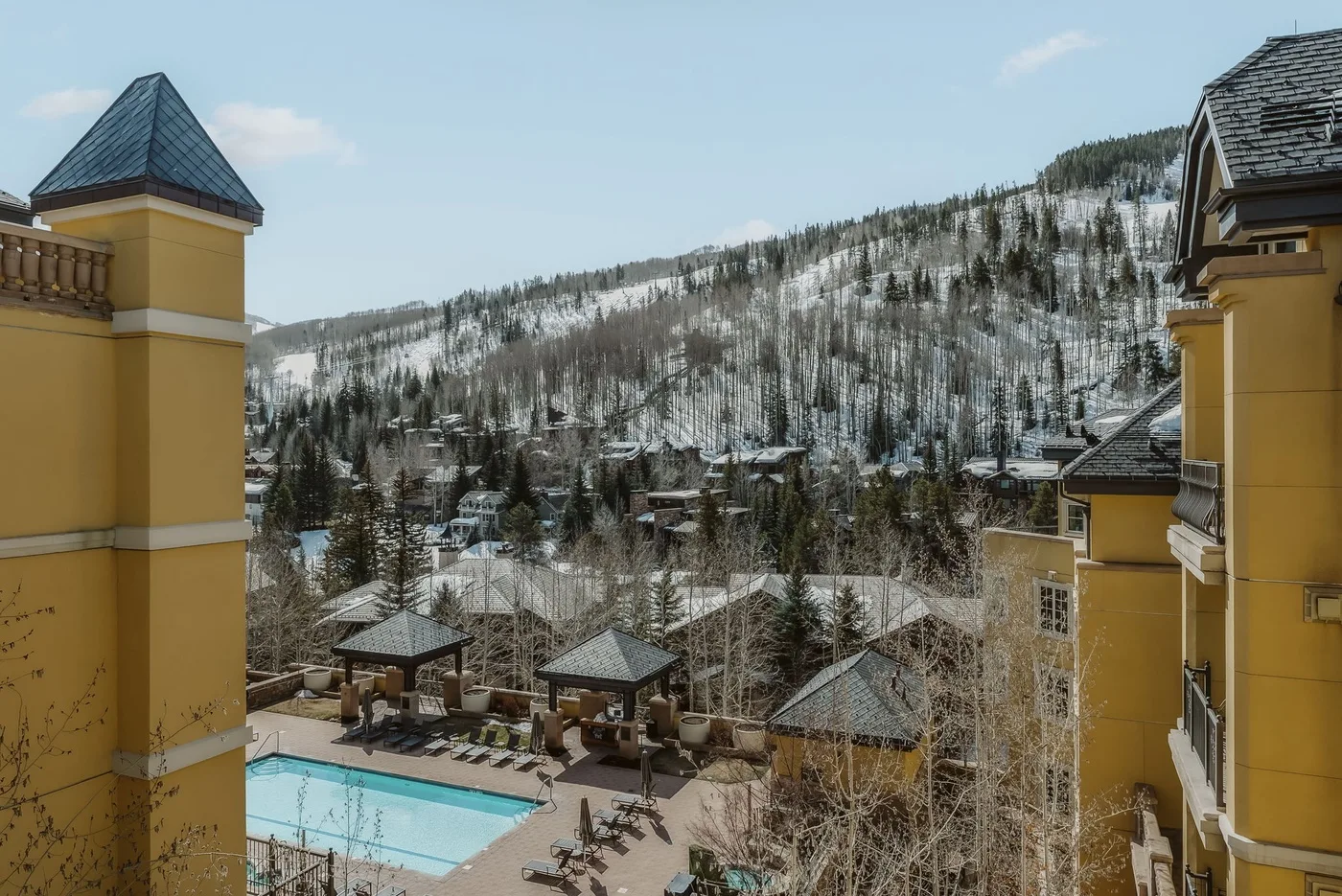 A mountain resort scene overlooks an outdoor pool and snow-dusted hillside.