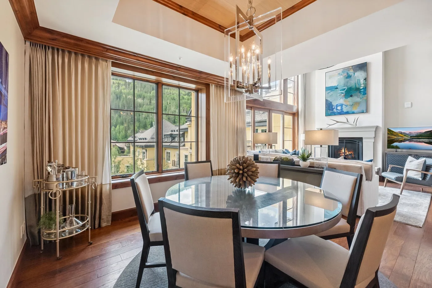 A bright dining area features a glass table beside large windows and a living space.